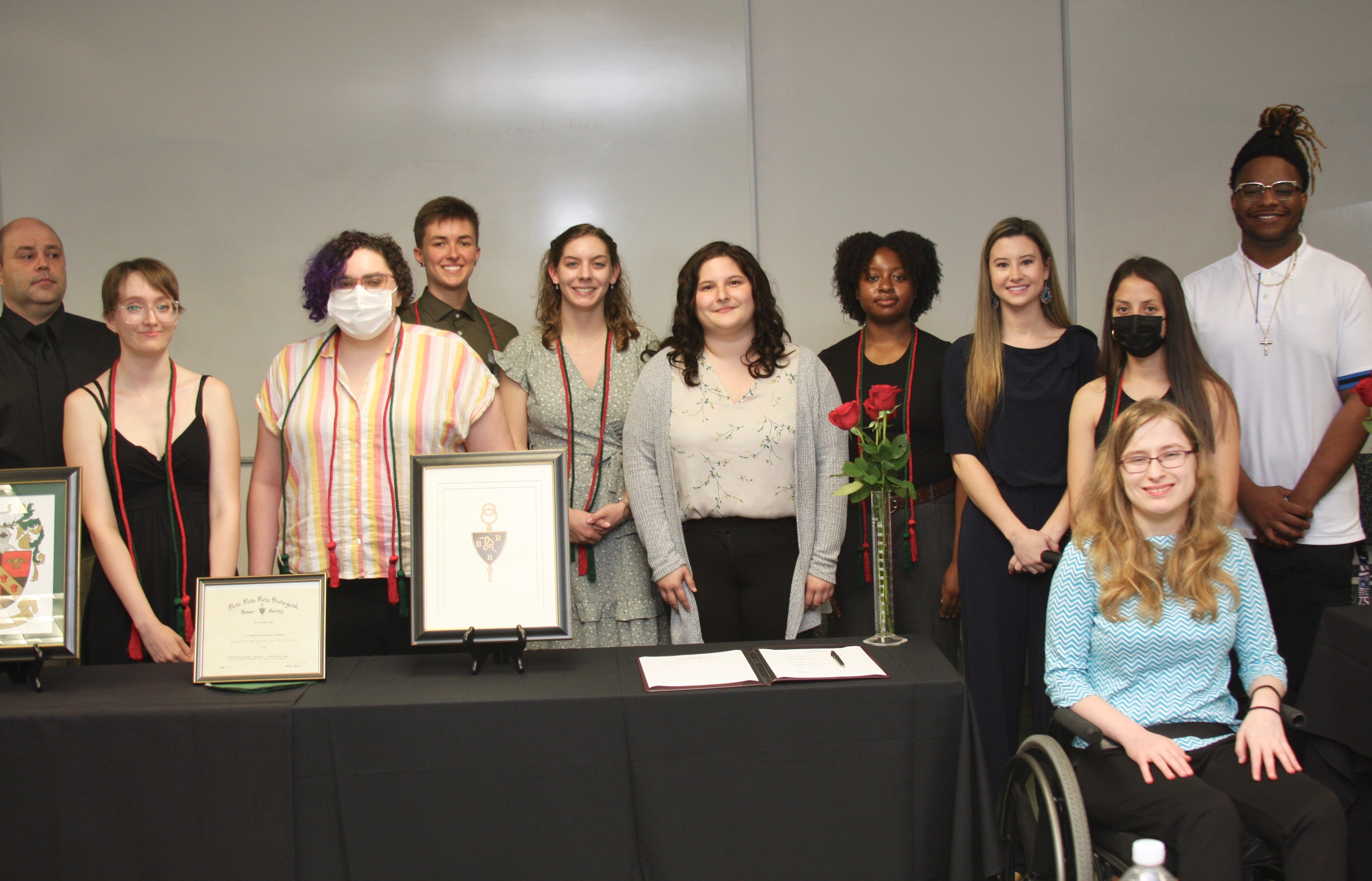 New and soon-to-be graduating members of TriBeta posing for a group picture standing behind a table with the TriBeta symbols