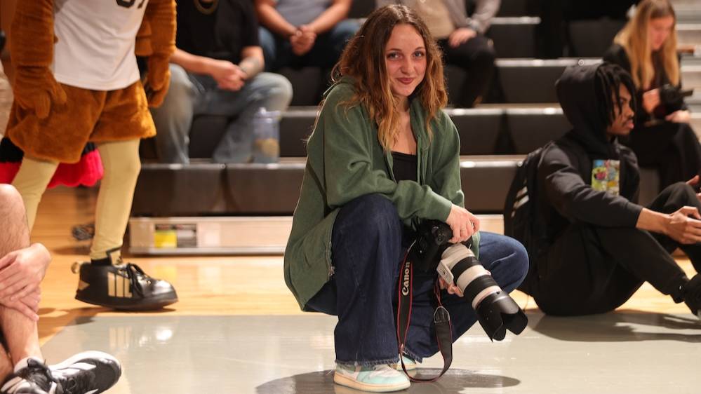 Michela Gritti kneels courtside at basketball game while holding a camera