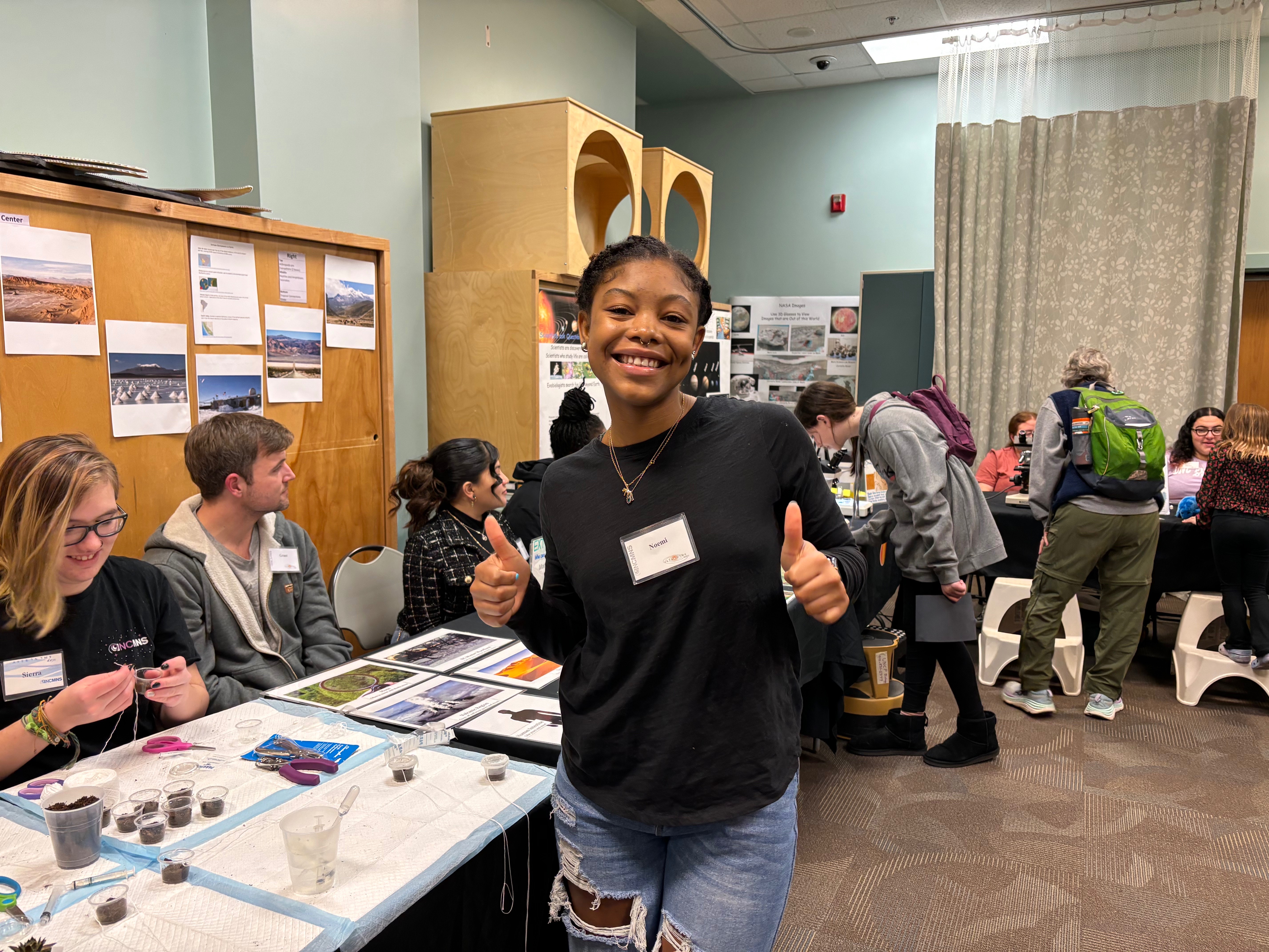 UNCP student Noemi smiles and holds two thumbs up at the NCAS booth.