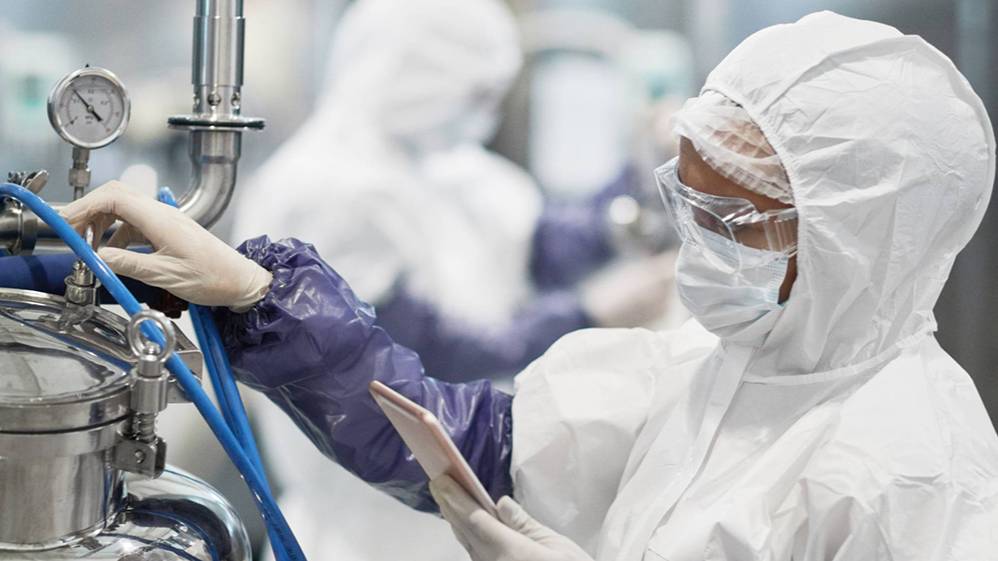 A technician in full protective cleanroom gear operates biopharmaceutical manufacturing equipment, representing the hands-on lab training offered through UNCP's free bioprocessing course.