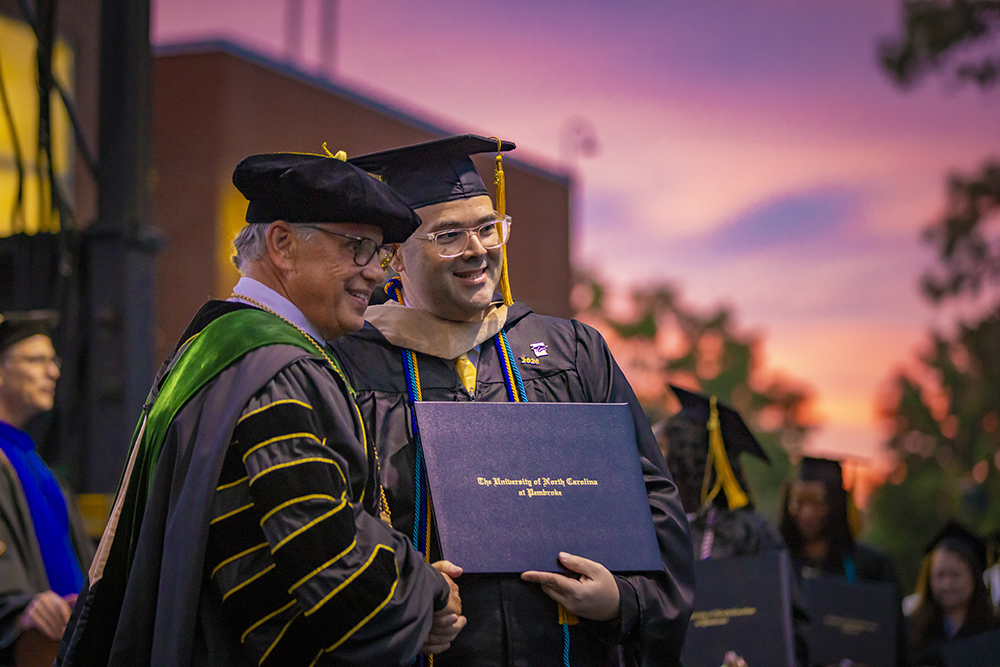Chancellor Robin Gary Cummings shakes a graduate's hand  during  the 2026 UNCP William Howard Dean Graduate School commencement ceremony.