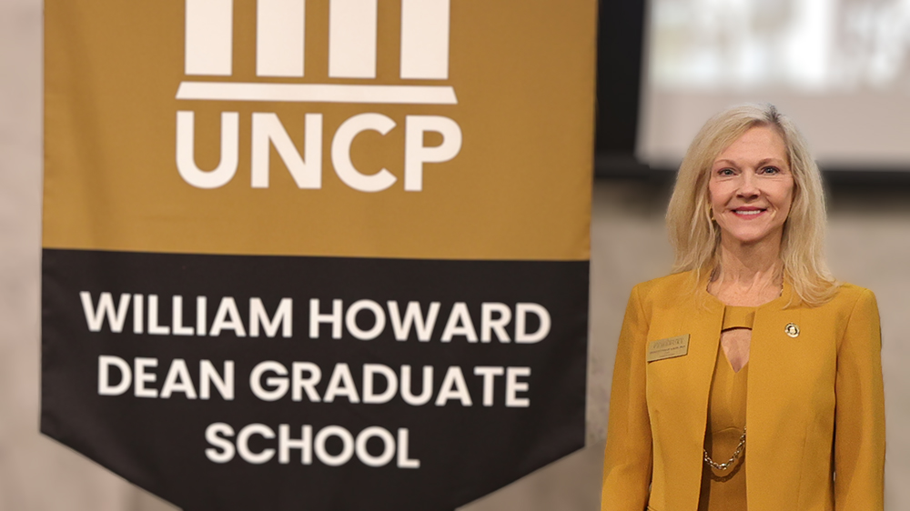 Dr. Irene Pittman Aiken, dean of the UNCP William Howard Dean Graduate School, stands alongside the Graduate School banner, representing her election to the Conference of Southern Graduate Schools Executive Board.