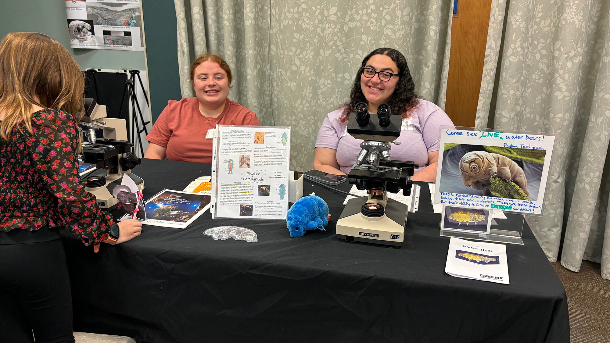 Two smiling college students set at a NCAS table at UNCP
