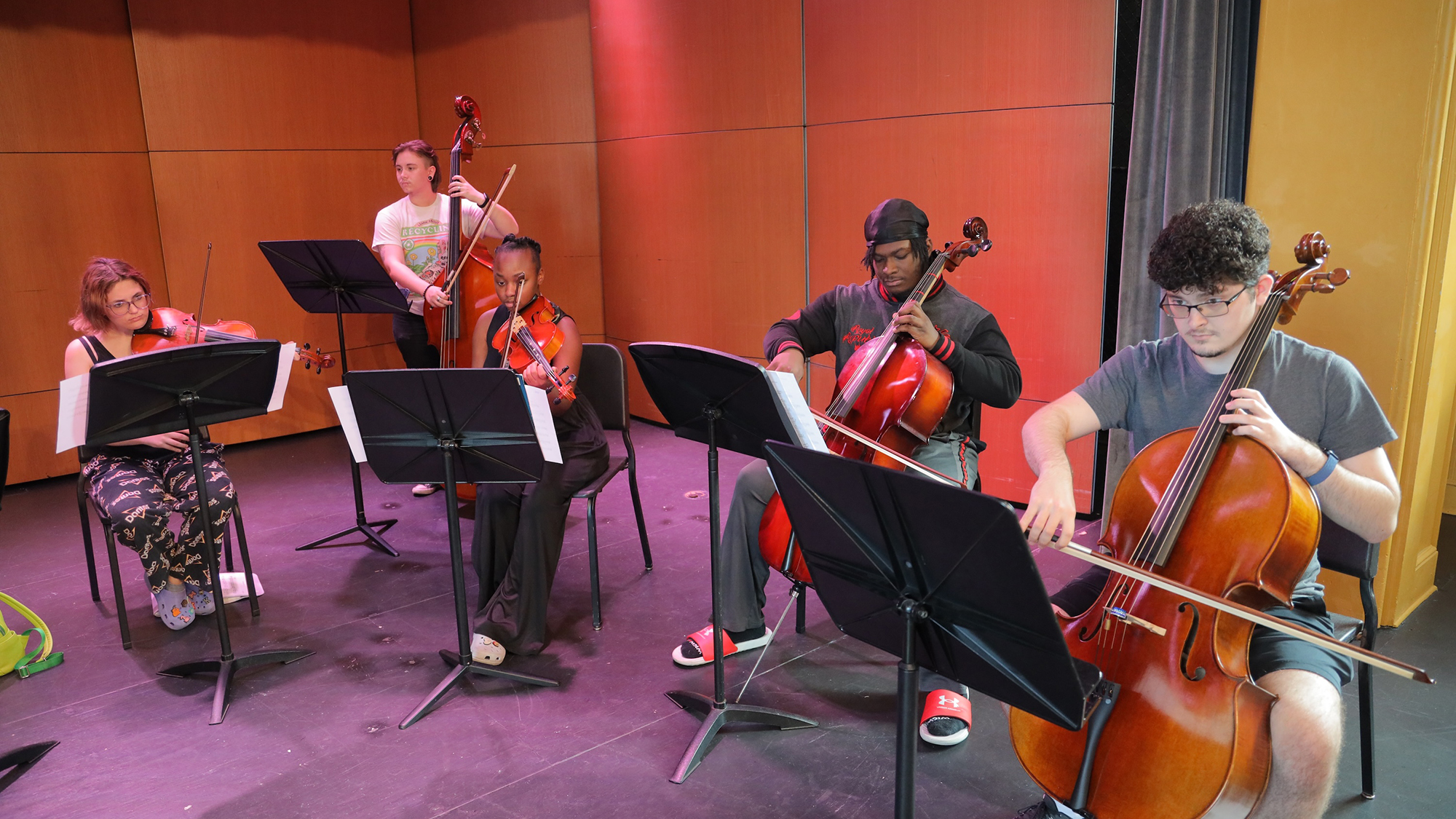 Orchestra students playing various instruments while reading sheet music