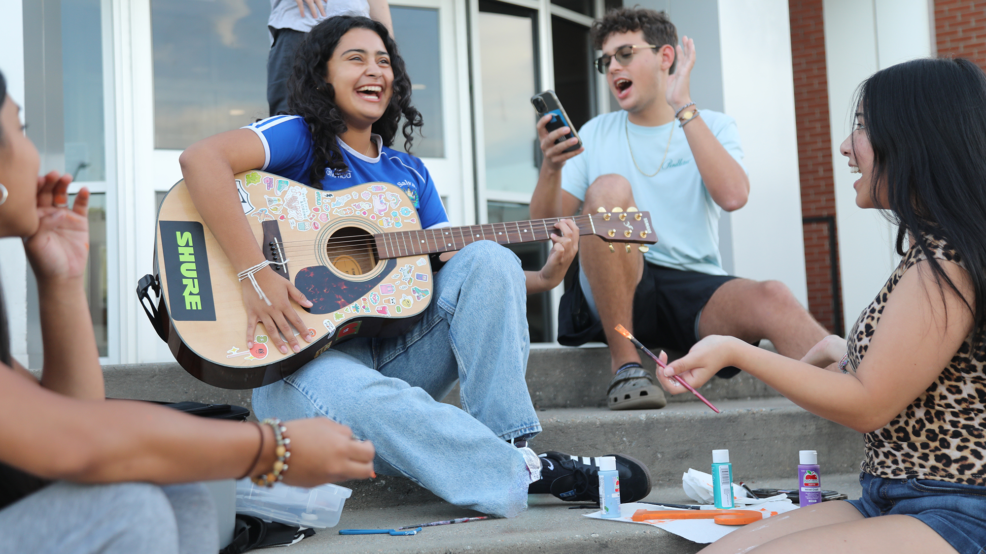UNCP students sitting on steps with a guitar and art supplies.