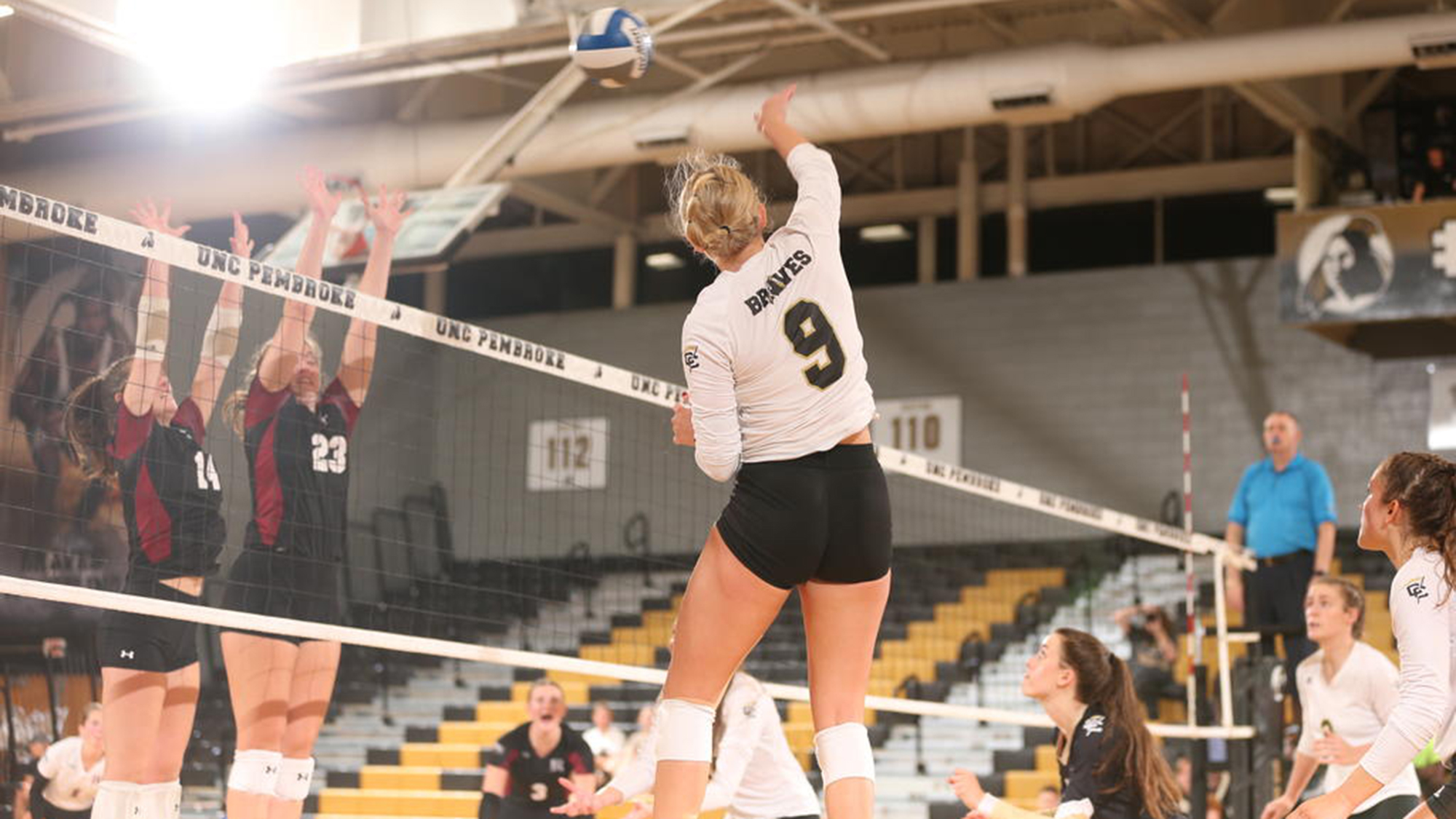 Woman wearing number 9 jersey is midair spiking a volleyball over the net.