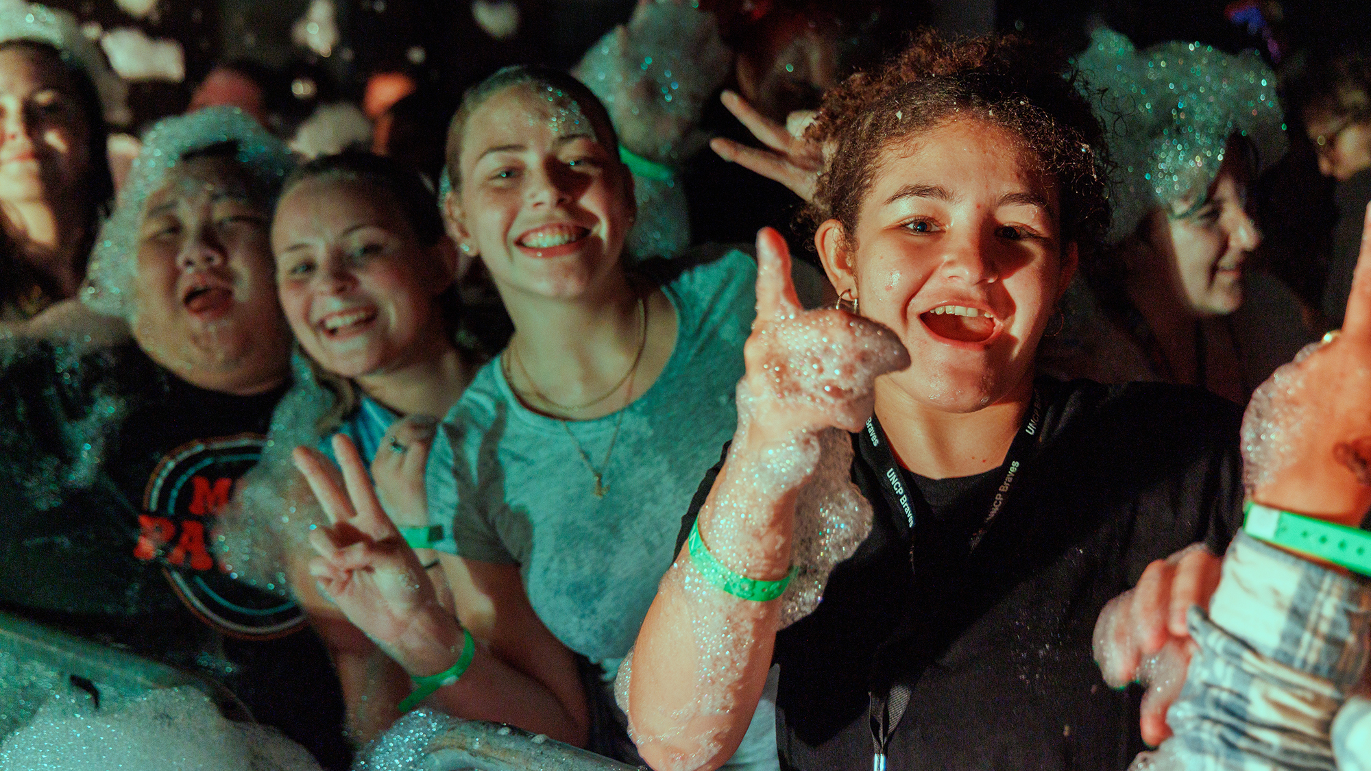 students covered in bubbles in night shot smiling and gesturing for the camera