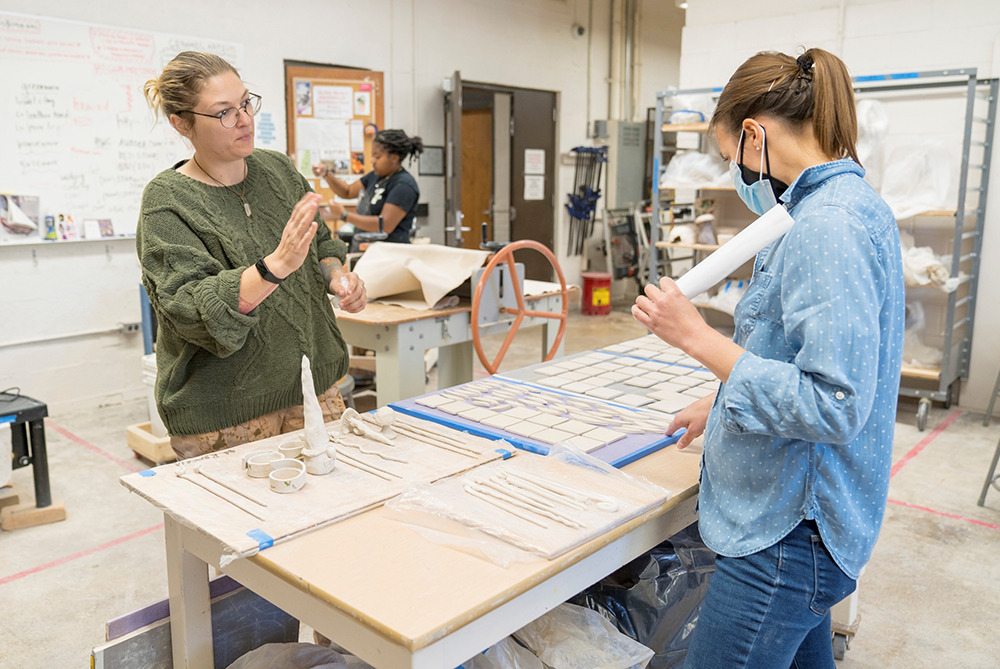 Professor talking with a senior pottery/ceramics student in the ceramics stuido in Locklear Hall at UNC Pembroke.