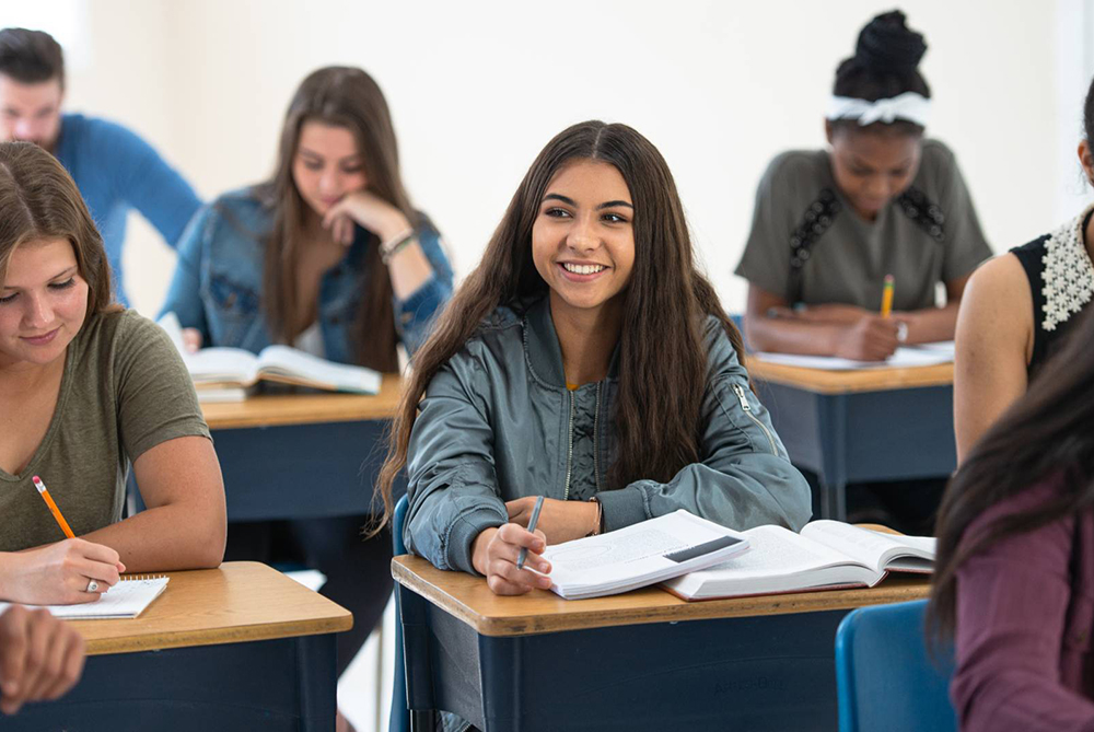student sitting at desk in class smiling at camera