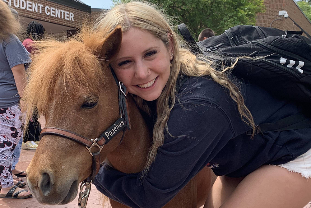 Student hugging a miniature horse or small pony outside the student center during finals week de-stress fest at UNC Pembroke.