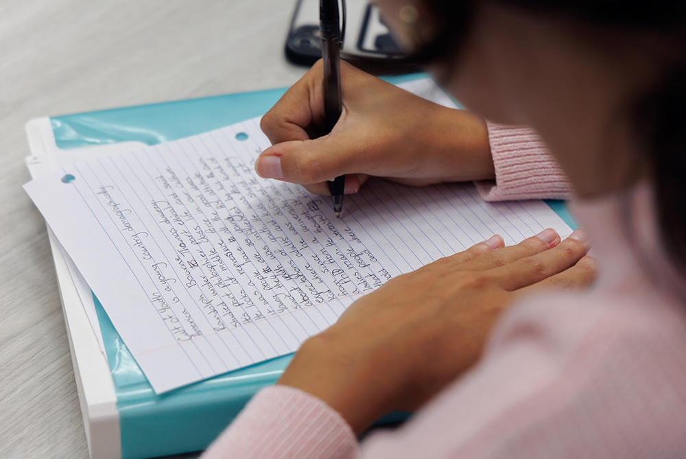 Female student hand writing a paper on lined notebook paper.