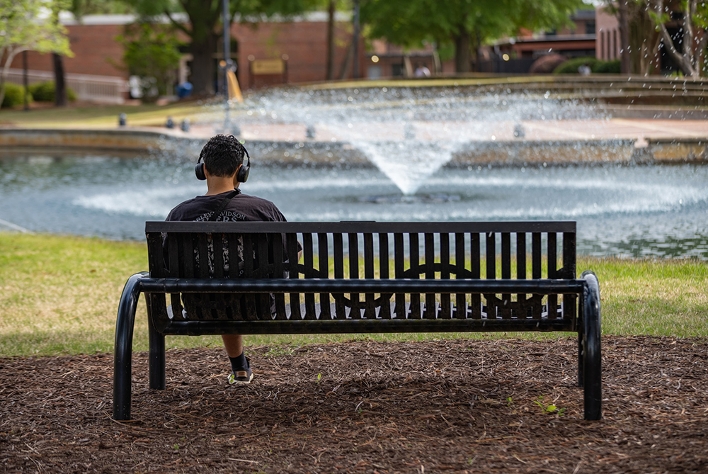 UNCP student sitting on bench looking at water feature