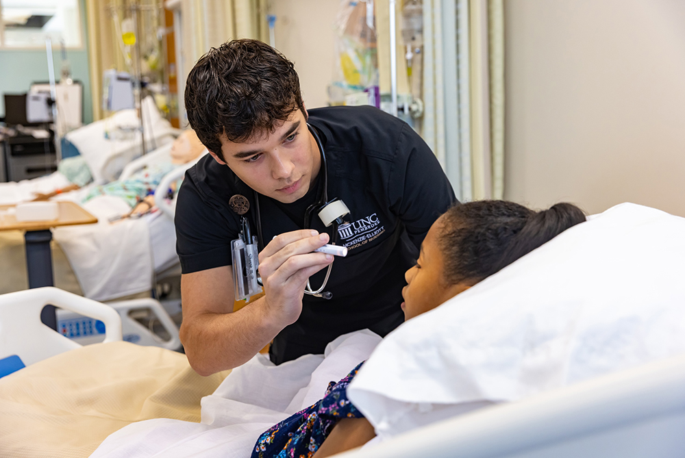 a male nursing student checking the eyes of a female patient lying in a hospital bed