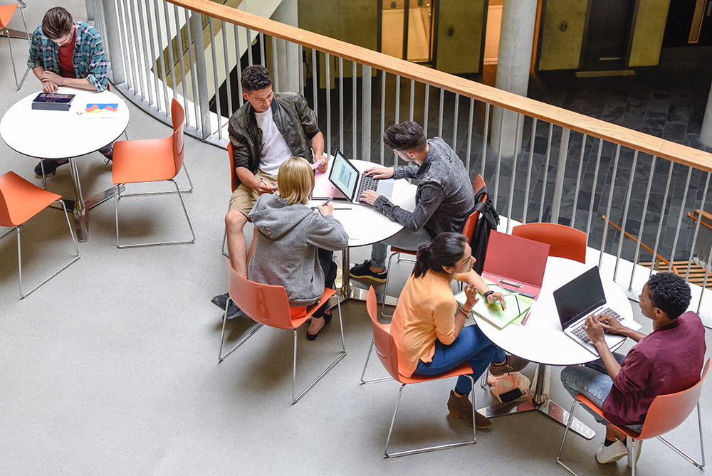 Students at balcony tables on laptops and talking
