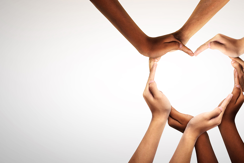 White backdrop with hands reaching in from out of frame coming together to form a heart with the shape of their fingers.