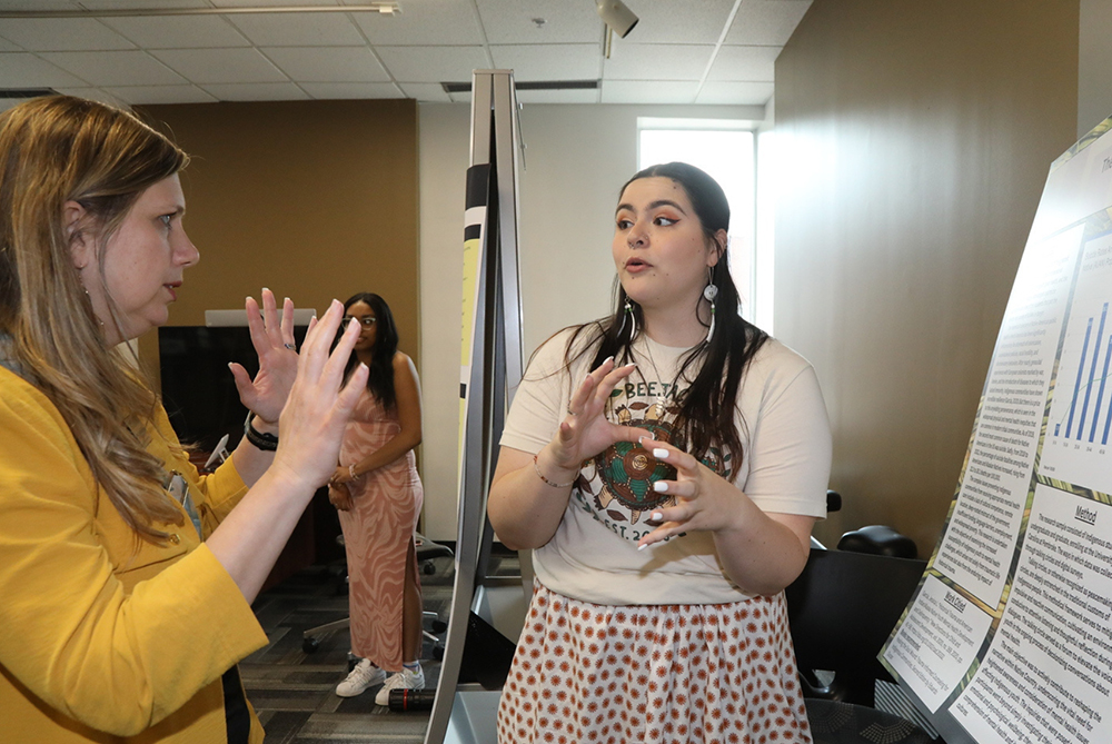 A female student presenting research,epresenting the REACH program at UNCP, emphasizing educational outreach, innovative research, and community impact.