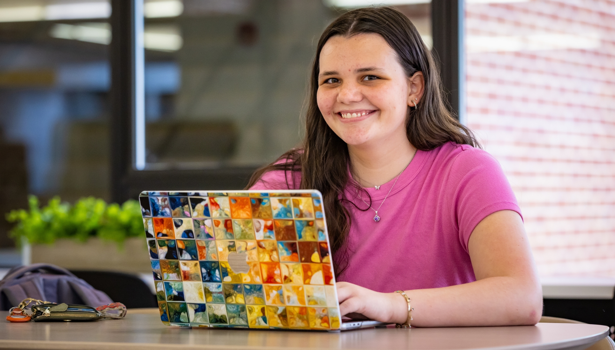 a girl sitting at a round table with a laptop sitting in front of her smiling.