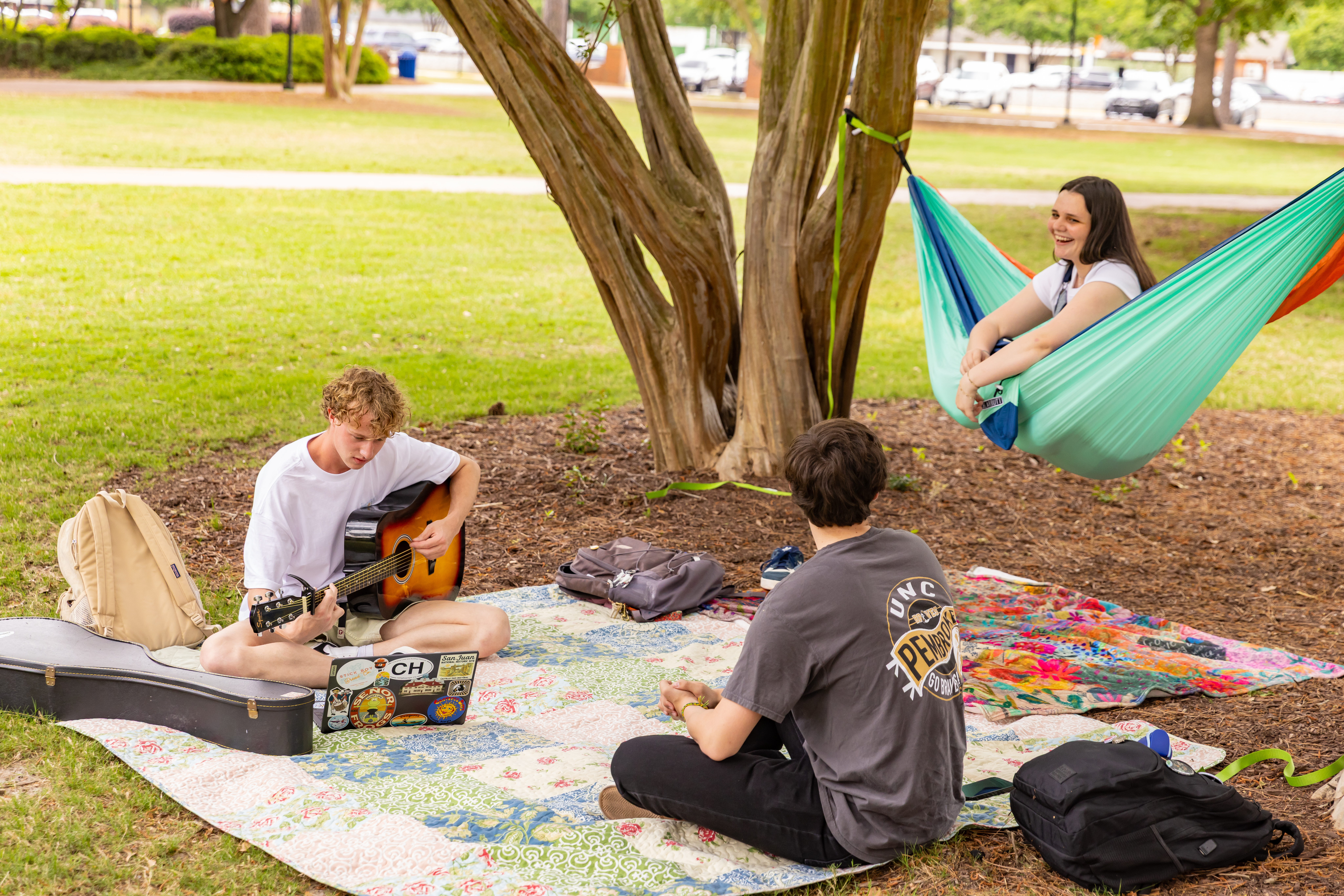 Students hanging out on the quad, playing guitar and sitting in a hammock