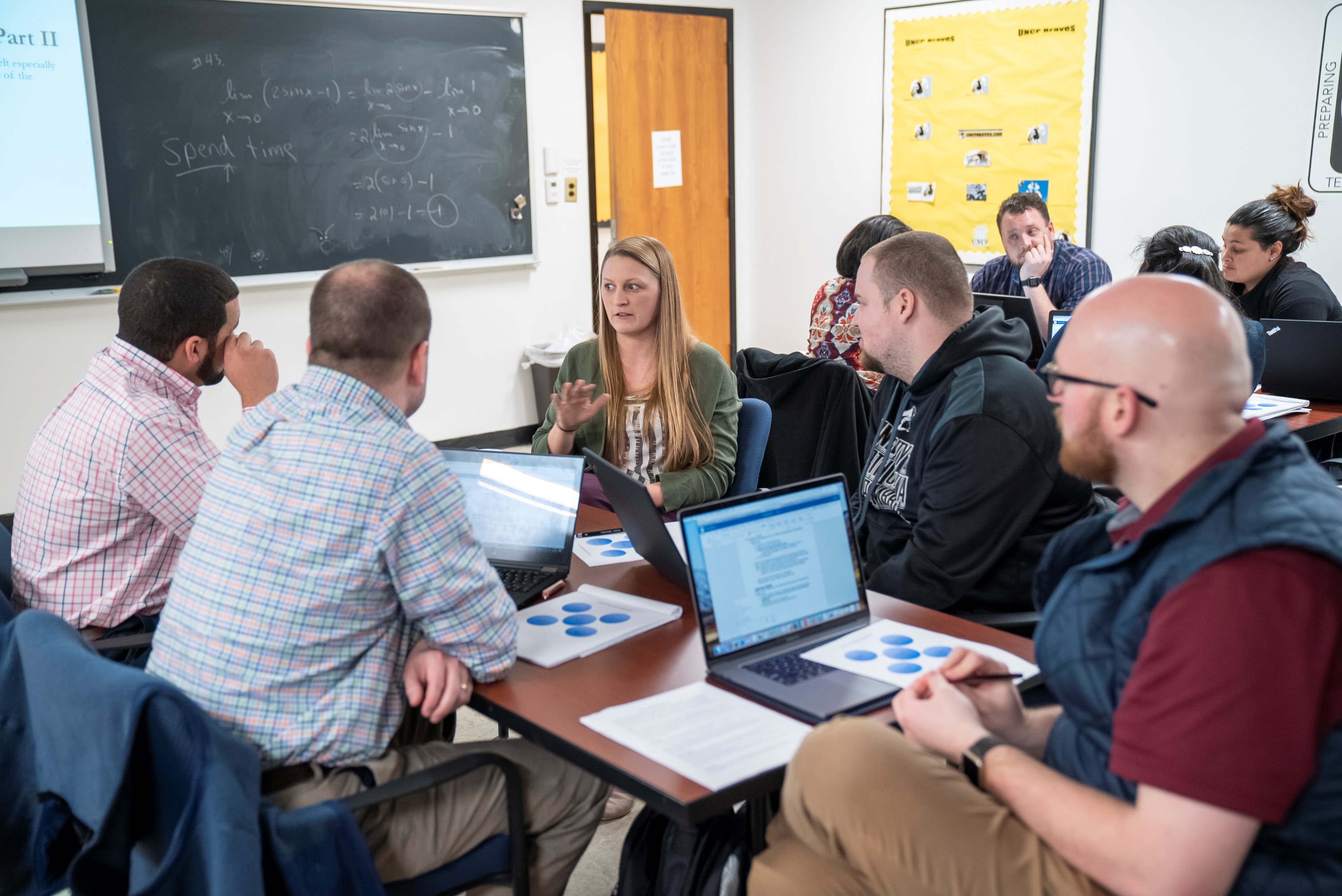 UNC Pembroke graduate students in education seated around a classroom table engaged in discussion.