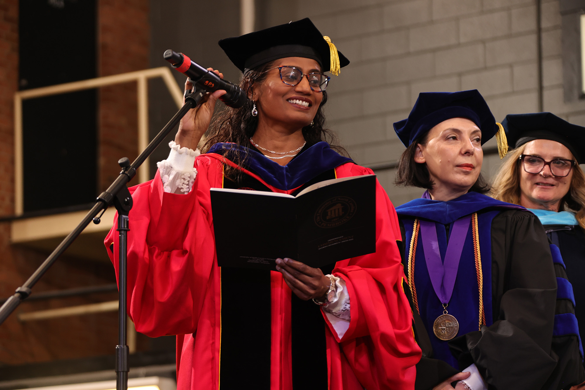 Three UNCP Deans in regalia stand on the stage at commencement
