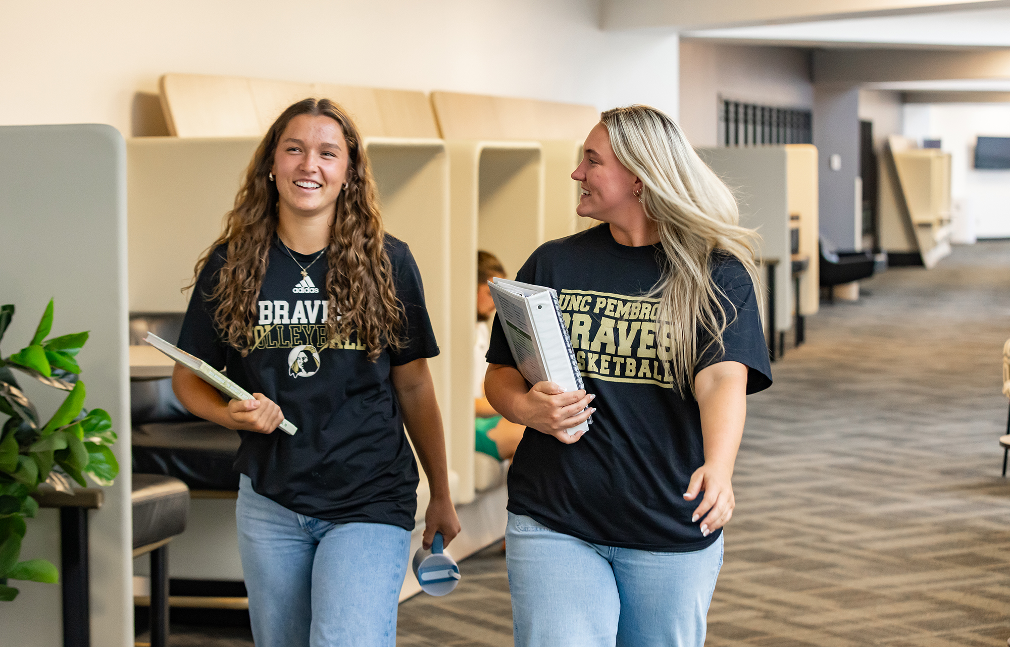 Two UNCP students walk together through a campus hallway, representing student resources and support services.